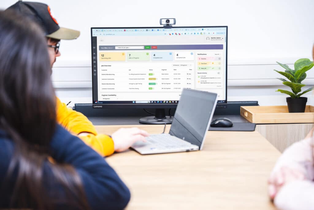 Software Developers using bespoke inspection software in the Red Box office sat at a desk with other team members